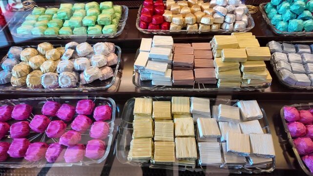 A vibrant assortment of colorful, wrapped chocolates arranged meticulously on display trays, showcasing a variety of hues and shapes in a candy store