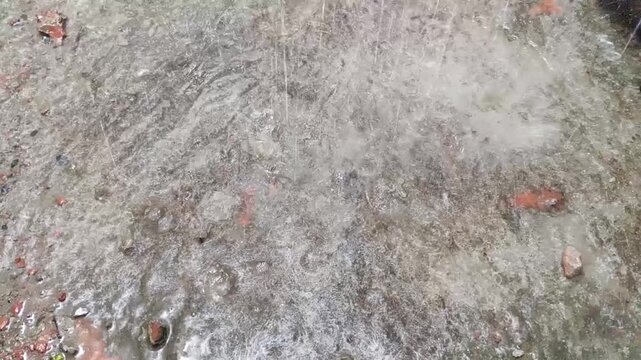 ​Heavy rain falling and splashing on a wet concrete surface with broken bricks