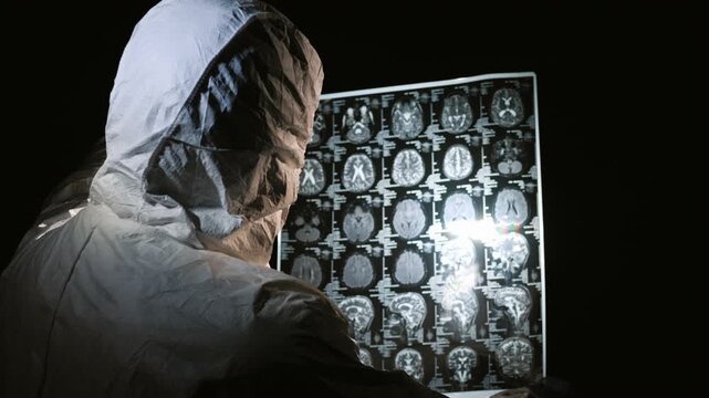 Scientist in biohazard suit analyzing brain magnetic resonance imaging scan in dark laboratory.