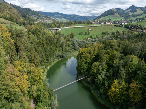 Aerial view of Lac de Montsalvens surrounded by dense forests, rolling hills, and a suspension bridge crossing the calm water in Gruyere District, Fribourg, Switzerland.