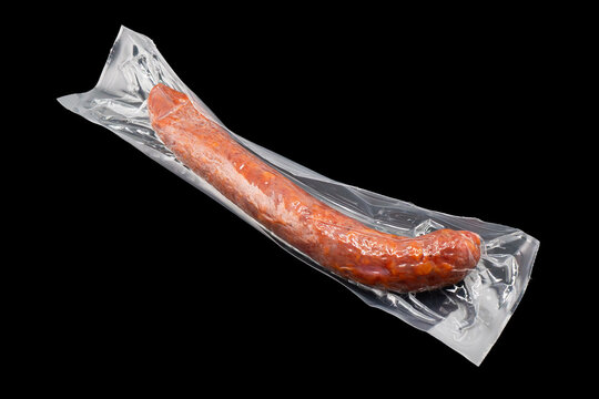 Sausages in vacuum plastic packaging isolated on black background. Vacuum transparent packaging with fresh sausages. A pack of sausages in a vacuum isolated.
