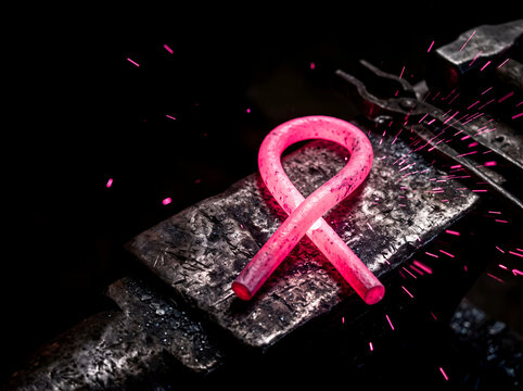 Glowing pink forged iron breast cancer awareness ribbon on anvil