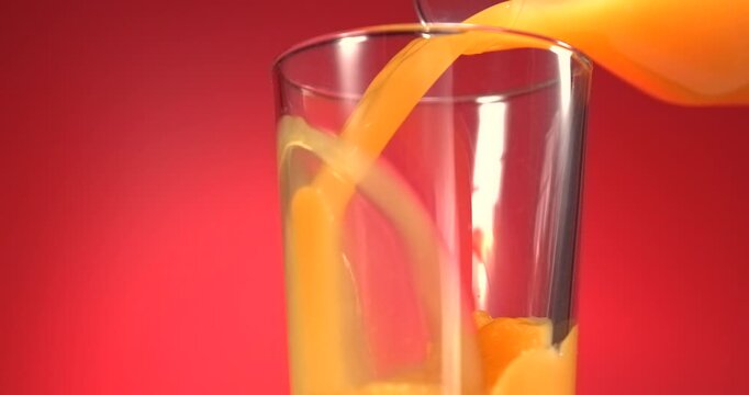 Fruit juice pouring from bottle into glass in slow motion on red background