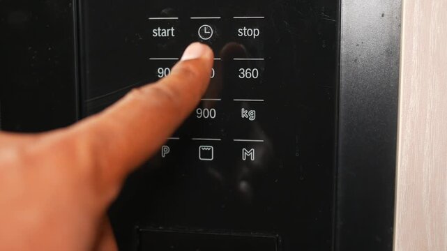 Close-up of finger pressing buttons on black microwave oven control panel with display.