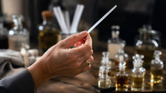 Woman holding a fragrance testing strip surrounded by glass perfume bottles during scent selection