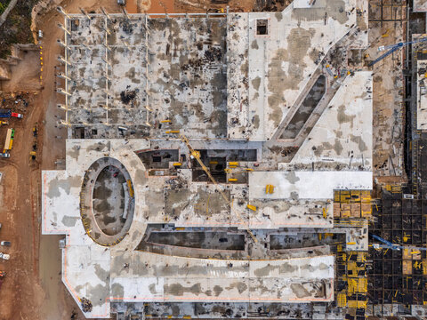 Aerial view of a large concrete construction site featuring an oval courtyard, structural columns, and yellow cranes in Santo Domingo Este, Santo Domingo Provinc, Dominican Republic.