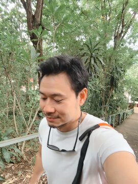 Smiling Asian Man Taking a Selfie While Exploring a Lush Green Park in Thailand