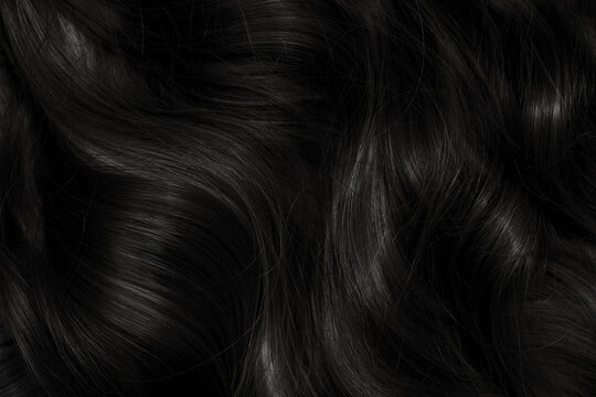 Brunette or black hair. Female long dark hair in black. Beautifully laid curls. Closeup texture in a dark key. Hairdressing, hair care and coloring. Shading gray hair. Background with copy space.