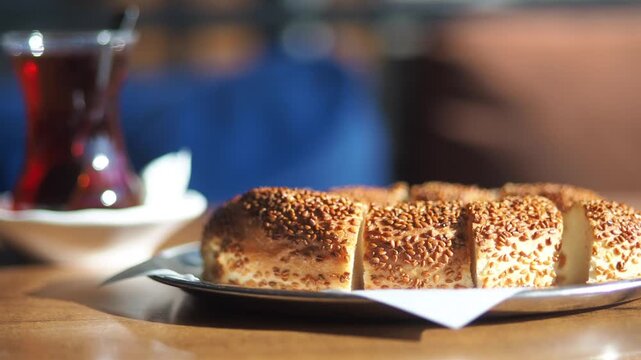Freshly sliced turkish simit bread with sesame seeds on silver plate near hot tea in cafe.