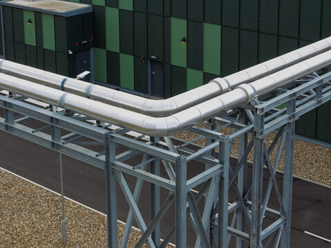 Aerial view of industrial pipes running along a metal support structure next to a modern data center building with a green and black patterned facade in the United Kingdom.
