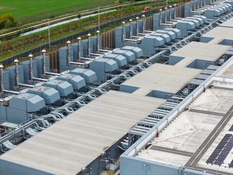 Aerial view of a large data center facility featuring rows of industrial cooling units, HVAC systems, and solar panels on the flat rooftops, United Kingdom.