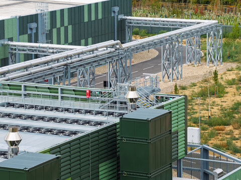 Aerial view of a modern data center facility featuring green-paneled walls, industrial cooling fans on the roof, and complex metal piping infrastructure in the United Kingdom.