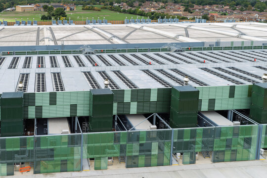 Aerial view of a modern data center facility featuring large cooling units on the roof and green architectural screening panels in the United Kingdom.