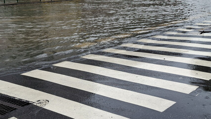 Zebra pedestrian crosswalk submerged in floodwater on city asphalt street during heavy monsoon rainstorm © ice on earth