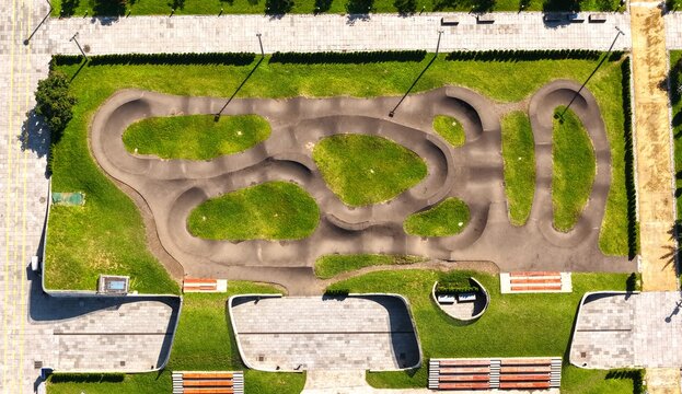 Aerial view of a pump track in a park with green grass, paved paths, and benches in Batumi, Adjara, Georgia.
