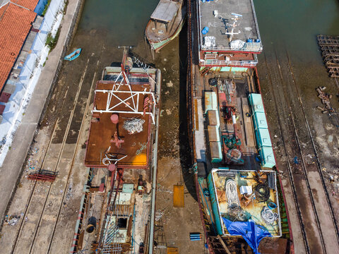 Aerial view of Sleko Port with fishing boats docked in the harbor, showing rusty decks, ropes, and industrial equipment in Cilacap, Central Java, Indonesia.