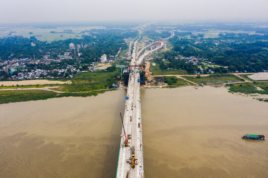 Aerial view of the Padma Bridge under construction spanning the river with heavy machinery and surrounding landscape in Mawa, Dhaka Division, Bangladesh.