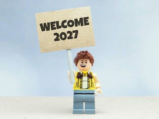 Obraz premium Indonesia - June 12, 2026 : Mini toy of action figure at table with blurred background. Miniature photography concept design. Minifigure of people with HAPPY NEW YEAR 2027 text at poster banner.
