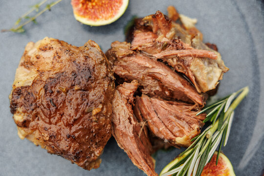 Close-up of tender cooked lamb pieces with a browned crust, garnished with rosemary and fresh figs on a ceramic plate