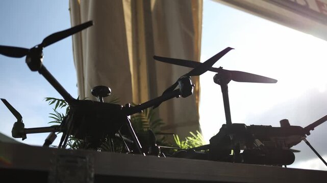 Military multirotor drones displayed in dramatic backlight showing unmanned aerial technology developed for reconnaissance surveillance and tactical field operations