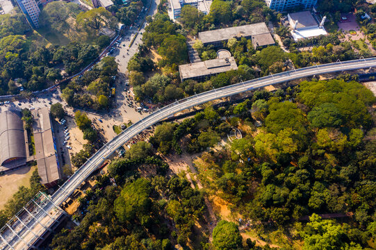 Aerial view of the elevated metro rail track winding through the lush green urban landscape and busy streets of Dhaka, Dhaka Division, Bangladesh.