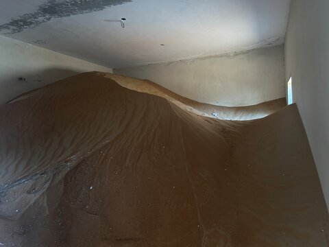 A surreal and shocking view of a deserted room completely overtaken by a massive sand dune inside a building, showing nature reclaiming space