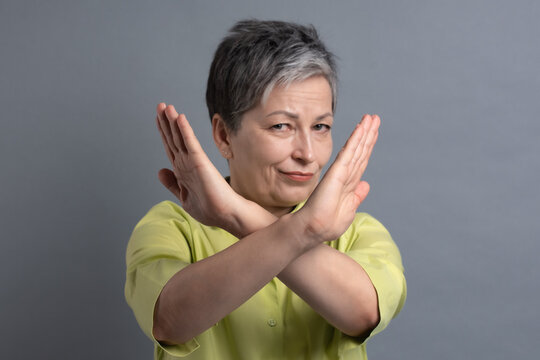 Serious mature woman showing stop sign crossing arms as gesture of rejection and prohibition