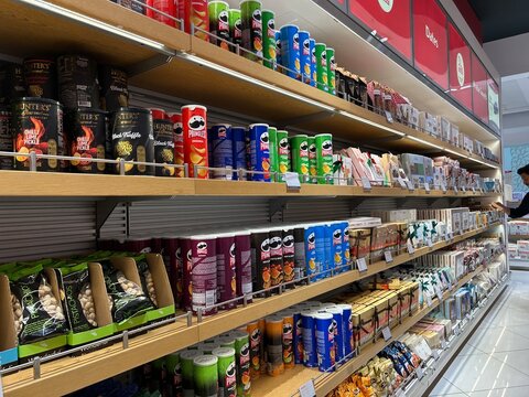 Stock image of supermarket shelves filled with various snack products including Pringles cans and pistachio bags in a retail store interior