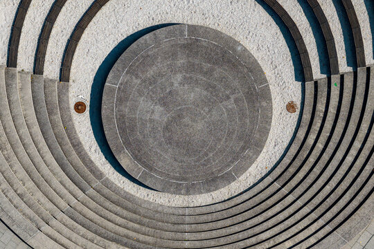 Aerial view of a circular stone amphitheater with concentric steps and a central platform surrounded by white gravel in Poland.