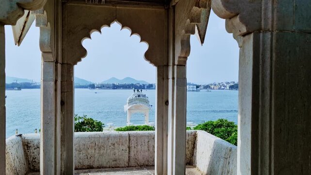 Scalloped arches and stone pillars frame a small pavilion and Lake Pichola at Jag Mandir in Udaipur.