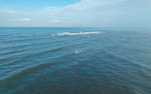 Aerial view of a small traditional boat with fishermen returning from the sea across the calm blue ocean waters in Kecamatan Jembrana, Bali, Indonesia.