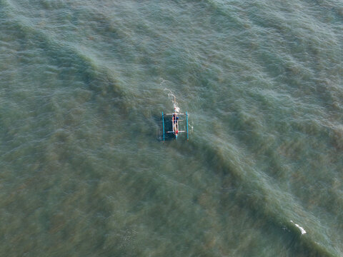 Aerial view of fishermen in a traditional outrigger boat returning from the sea across the gentle waves in Kecamatan Jembrana, Bali, Indonesia.