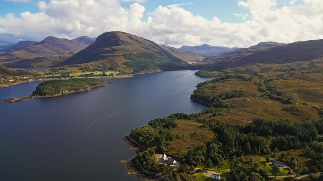 Aerial view of Scottish Highlands lakeside with rolling hills. Mountains flank calm waters under cloudy skies. Greenery and small cottages line the shore. Scene peaceful, serene, perfect for travel or
