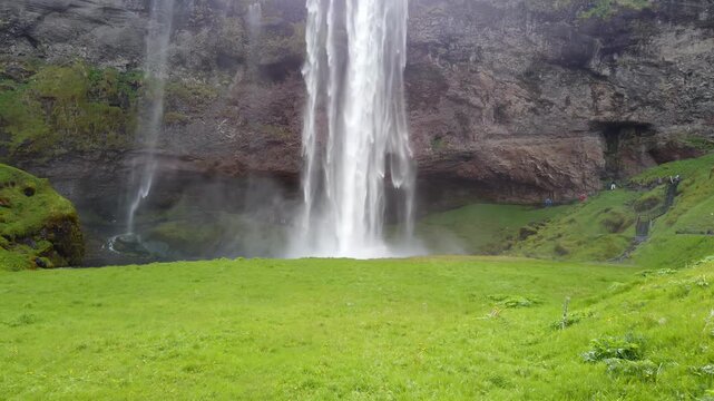 Seljalandsfoss waterfall, Iceland, plunging from an overhanging cliff onto a wide green lawn, with thin side streams falling beside it.