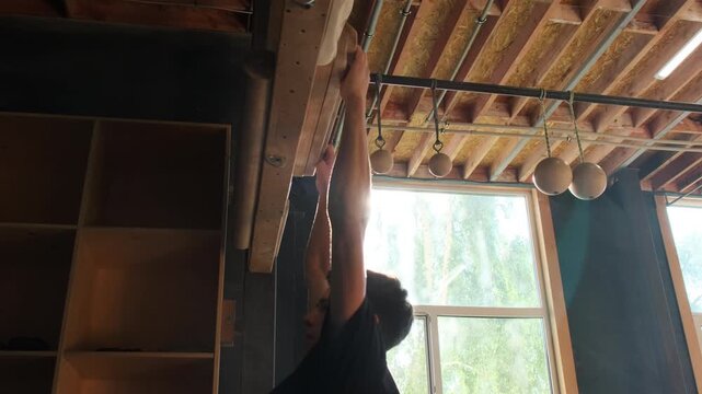 Man hangs on vertical board performing pull-up exercise in modern sports club. Strong man engages in workout improving endurance slow motion