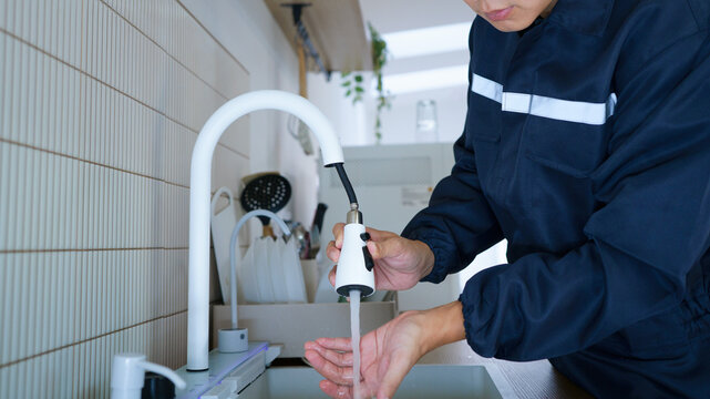 A plumber or maintenance worker in a navy uniform inspects a white pull down faucet sprayer, ideal for plumbing services and home repair concepts