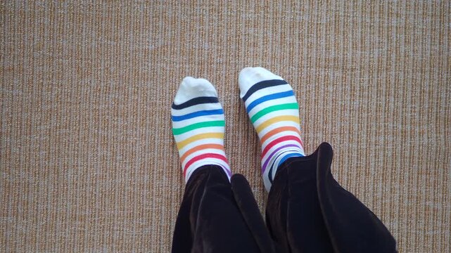 Feet wearing rainbow striped socks wiggle on beige carpet dynamic movement abstract.