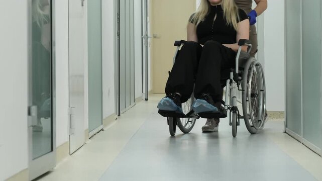 Young woman with mobility disability receives medical support from caregiver in hospital. Wheelchair care service and clinical assistance