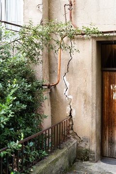 Crack in building caused by ground movement provoked by works at construction site or earthquake, deep structural damage in concrete residential building after natural disaster, facade destruction.