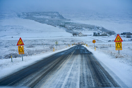 Driver's view of an icy snow-covered road trip in Iceland during winter with road signs and one-lane bridge. Scenic rural arctic driving experience.