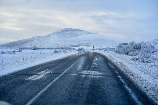 Driver point of view along icy asphalt road leading toward scenic snow-covered mountain in Iceland winter. Arctic highway road trip and travel adventure.