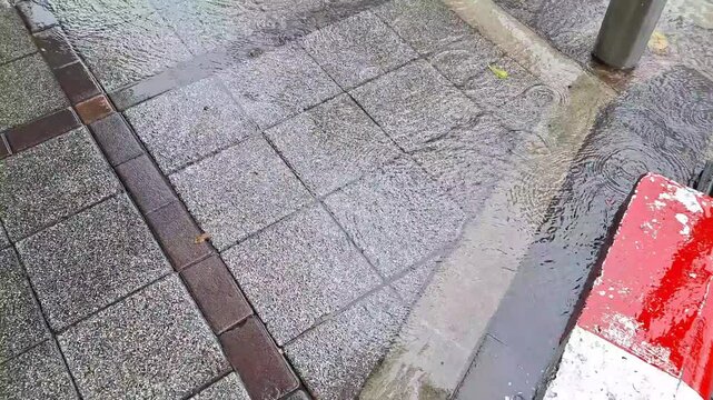 Rainwater flowing rapidly along city sidewalk curb during heavy monsoon rainstorm in urban area