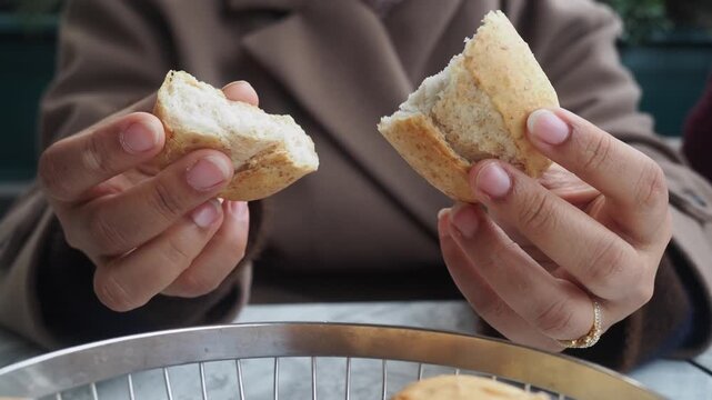 Woman breaks bread roll in half to share at outdoor cafe table footage.