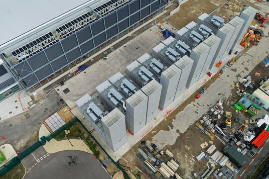 Aerial view of a data center featuring large industrial cooling units and HVAC systems on a concrete pad, with construction materials and equipment in the United Kingdom.