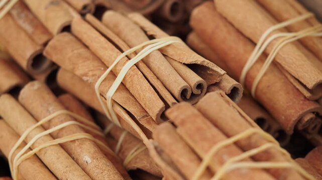 Bundled cinnamon sticks rotating in wooden container showcasing texture and organic shape.