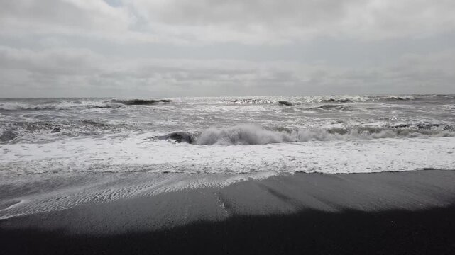 Reynisfjara black sand beach near Vik, Iceland, rough Atlantic waves rolling onto the dark shore under a grey sky.