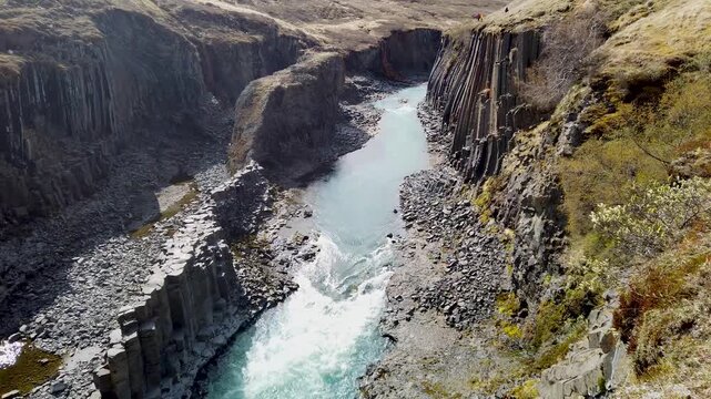 Studlagil canyon, Iceland, a glacial river with turquoise water rushing between walls of hexagonal basalt columns, seen from above on a sunny day.