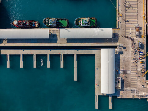 Aerial view of Nassau Cruise Port with tugboats docked at the pier, white canopy structures, and pedestrian walkways in Nassau, The Bahamas.