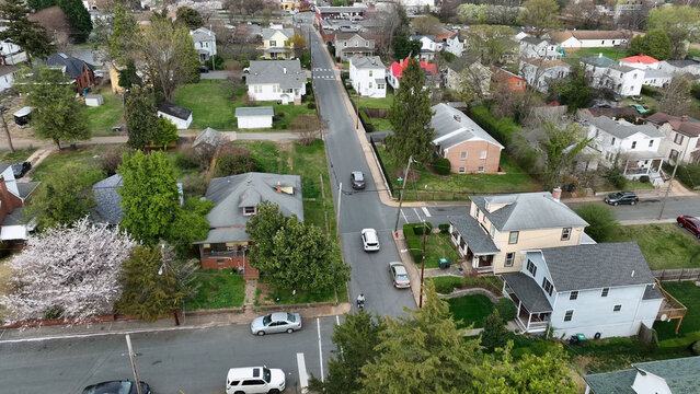 Aerial view of a residential neighborhood with houses, lush trees, and cars driving along a street in Charlottesville, Virginia, United States.