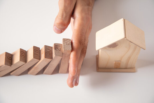 Male hand stopping wooden blocks from falling on house.
